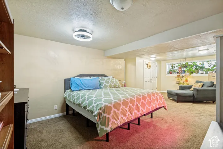 Carpeted room with a built-in wooden shelving unit, ceiling-mounted light fixture, and a window with natural light