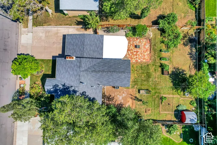 Asphalt shingle roofing, paved driveway, expansive lawn, mature trees, and a flagstone patio area