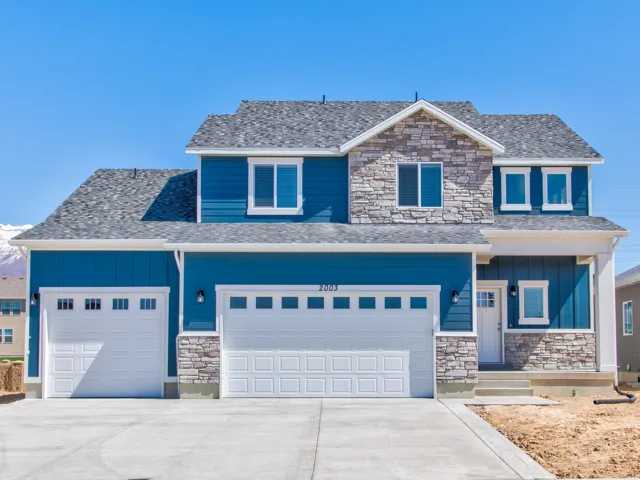Two-story residence featuring a stone and siding exterior, multi-pane windows, dual garage doors, and an asphalt shingle roof