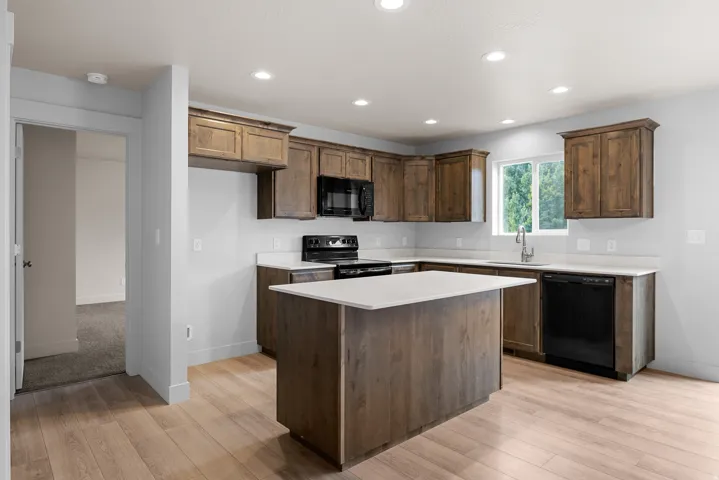 Kitchen featuring wood-finish flooring, an island with countertop, perimeter cabinetry, light-toned countertops, and recessed lighting