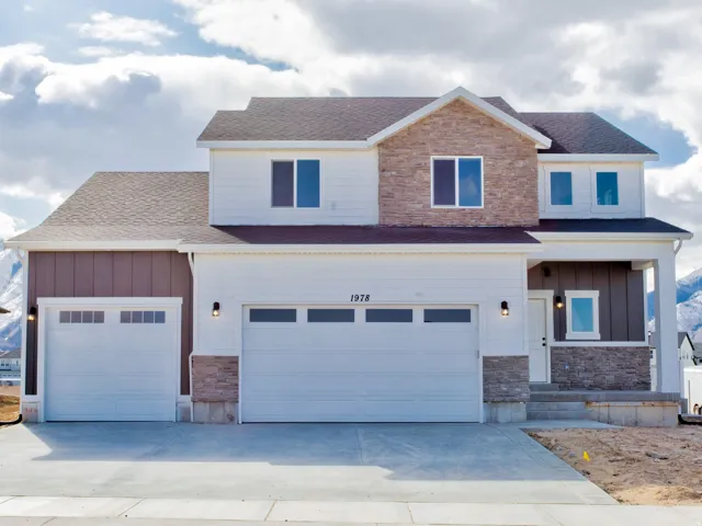 Two-story residence featuring a multi-tone exterior, attached two-car garage, and a covered entry
