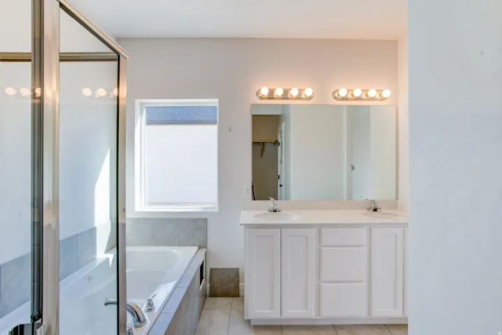 Dual vanity with white cabinetry, a large mirror, and overhead lighting