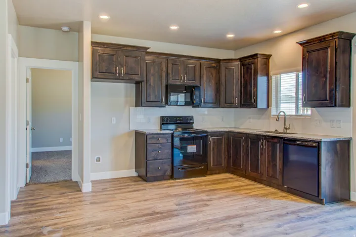 Kitchen featuring dark wood-finish cabinetry, granite-style countertops, an undermount sink, a subway tile backsplash, and wood-finish flooring