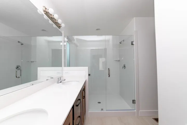 Double vanity with integrated sinks, white countertops, dark wood-finish cabinetry, and a glass-enclosed shower