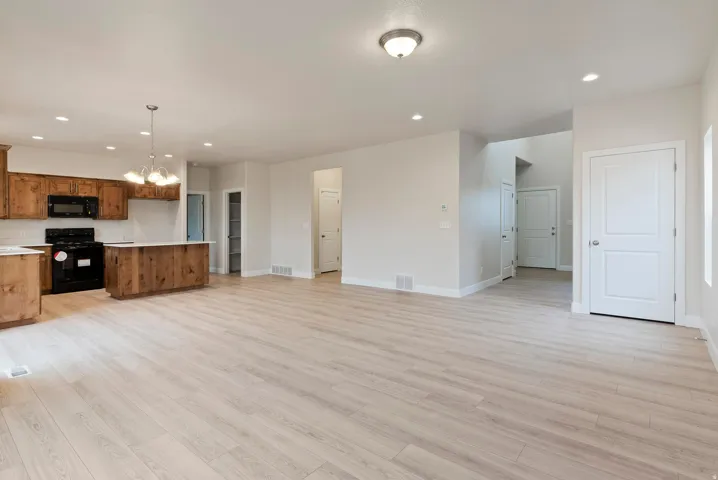 Open-concept living space with light wood-finish flooring, recessed lighting, and a kitchen featuring wood cabinetry, white countertops, and a central island with a pendant light fixture