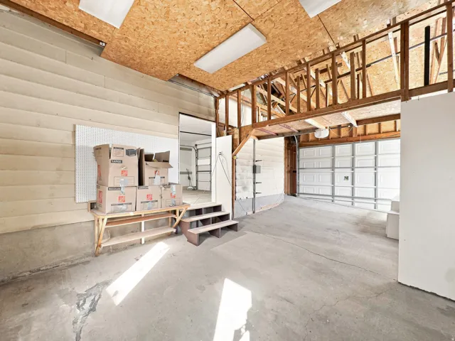 Concrete flooring with two overhead garage doors, exposed wood framing, and a wood-paneled wall