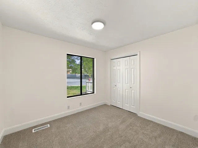 Neutral tone wall paint, flush mount ceiling light, carpet flooring, bi-fold closet doors, and a window with black trim