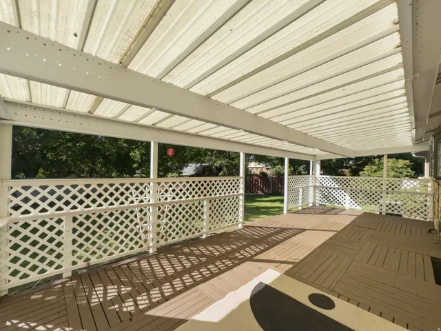 Expansive covered deck with lattice railing, wood-finish flooring, and a corrugated translucent roof