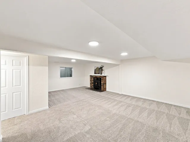 Spacious room with patterned carpet flooring, recessed lighting, and a brick-surround fireplace with a wood-burning stove