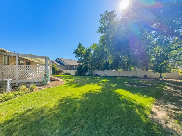 Expansive backyard featuring a covered deck, white lattice railing, mature trees, and a privacy fence