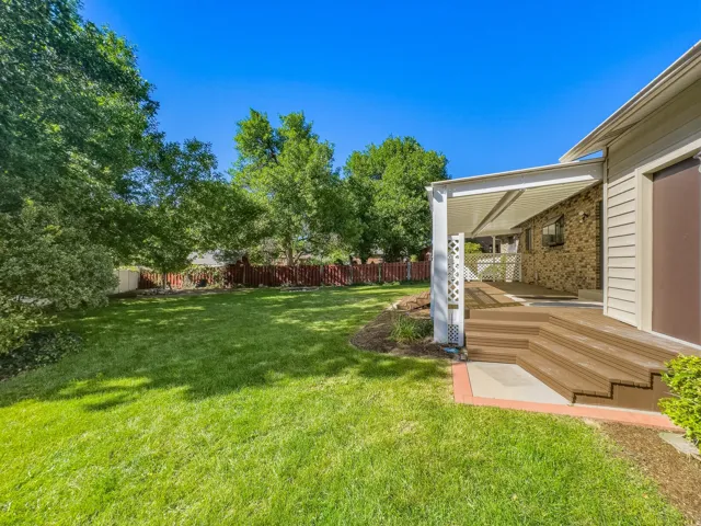 Expansive green lawn, multi-level composite deck, white lattice railing, covered patio, and mature trees