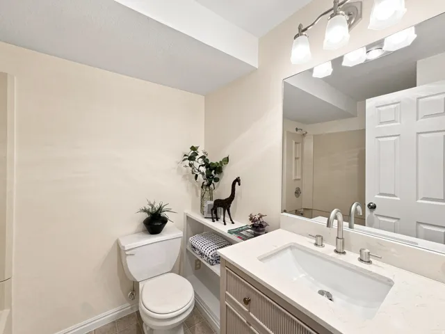 Vanity with integrated sink and brushed nickel faucet, large wall-mounted mirror, three-light vanity fixture, built-in shelving, and tiled flooring
