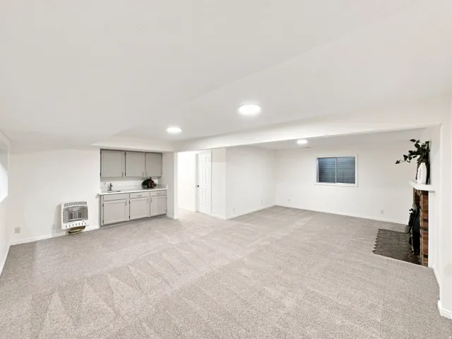 Expansive carpeted room featuring a built-in wet bar with cabinetry, a brick fireplace, a window with horizontal blinds, and recessed lighting