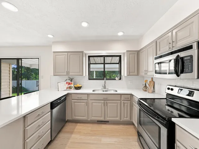 Kitchen featuring light-toned cabinetry, white countertops, stainless steel appliances, and wood-finish flooring