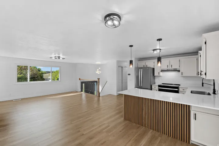 Wood-finish flooring throughout, white cabinetry with matte black hardware, stainless steel appliances, and a kitchen island with fluted wood paneling and a white countertop