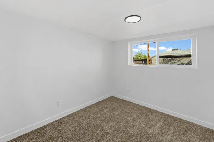 White walls with neutral carpeting, featuring a modern flush-mount ceiling light and a horizontal window