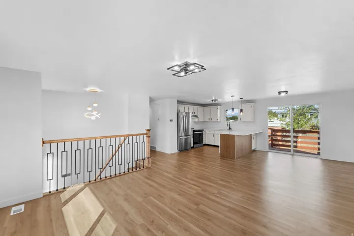 Open-concept living space featuring wood-finish flooring, a modern kitchen with white cabinetry and stainless steel appliances, and a sliding glass door