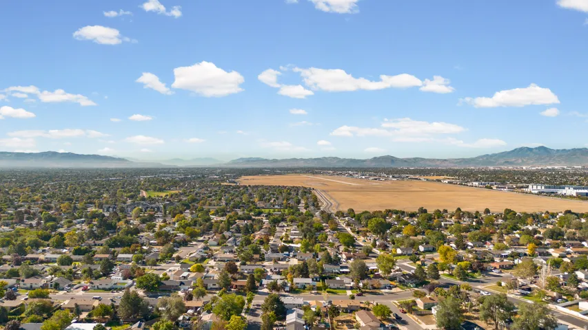 Expansive aerial perspective showcasing a residential area with mature tree coverage, a large open field, and distant mountain backdrops
