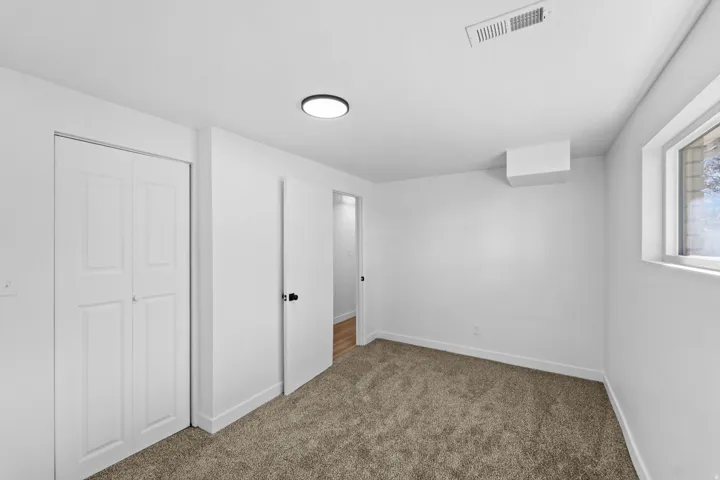 Plush carpeting, bright white walls, a built-in closet with bi-fold doors, and a window for natural light