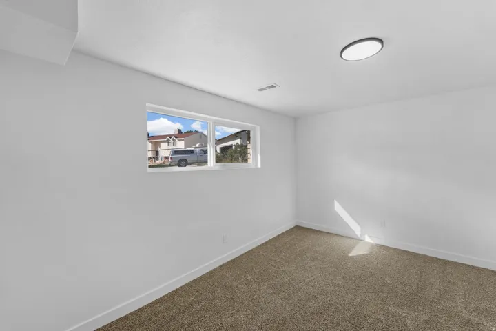 Recessed window, white painted walls, brown carpet flooring, and a flush-mount ceiling light