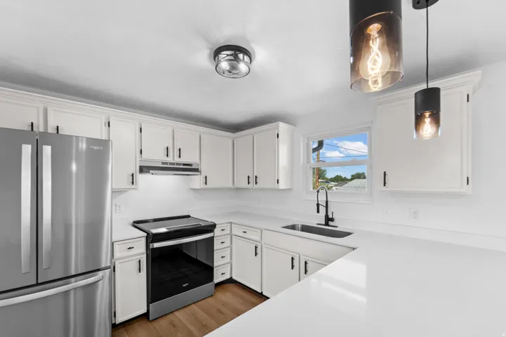 White cabinetry, stainless steel appliances, white countertops, wood-finish flooring, and modern pendant lighting