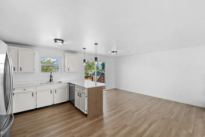 Open-concept space featuring wood-finish flooring, white cabinetry, a kitchen island with a slatted wood-finish panel, and stainless steel appliances