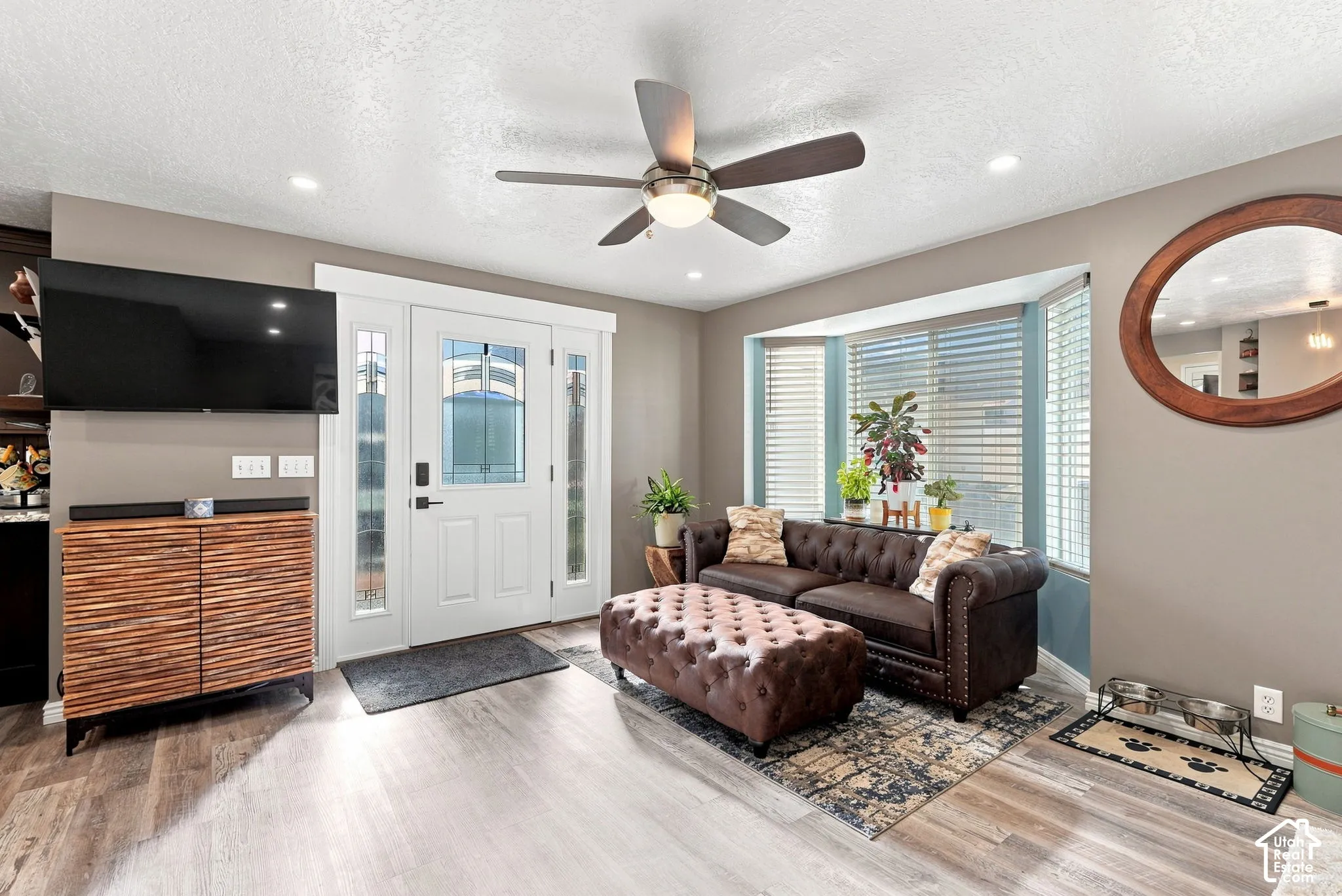 Recessed lighting, wood-finish flooring, a ceiling fan, a bay window with blinds, and a white entry door with frosted sidelights
