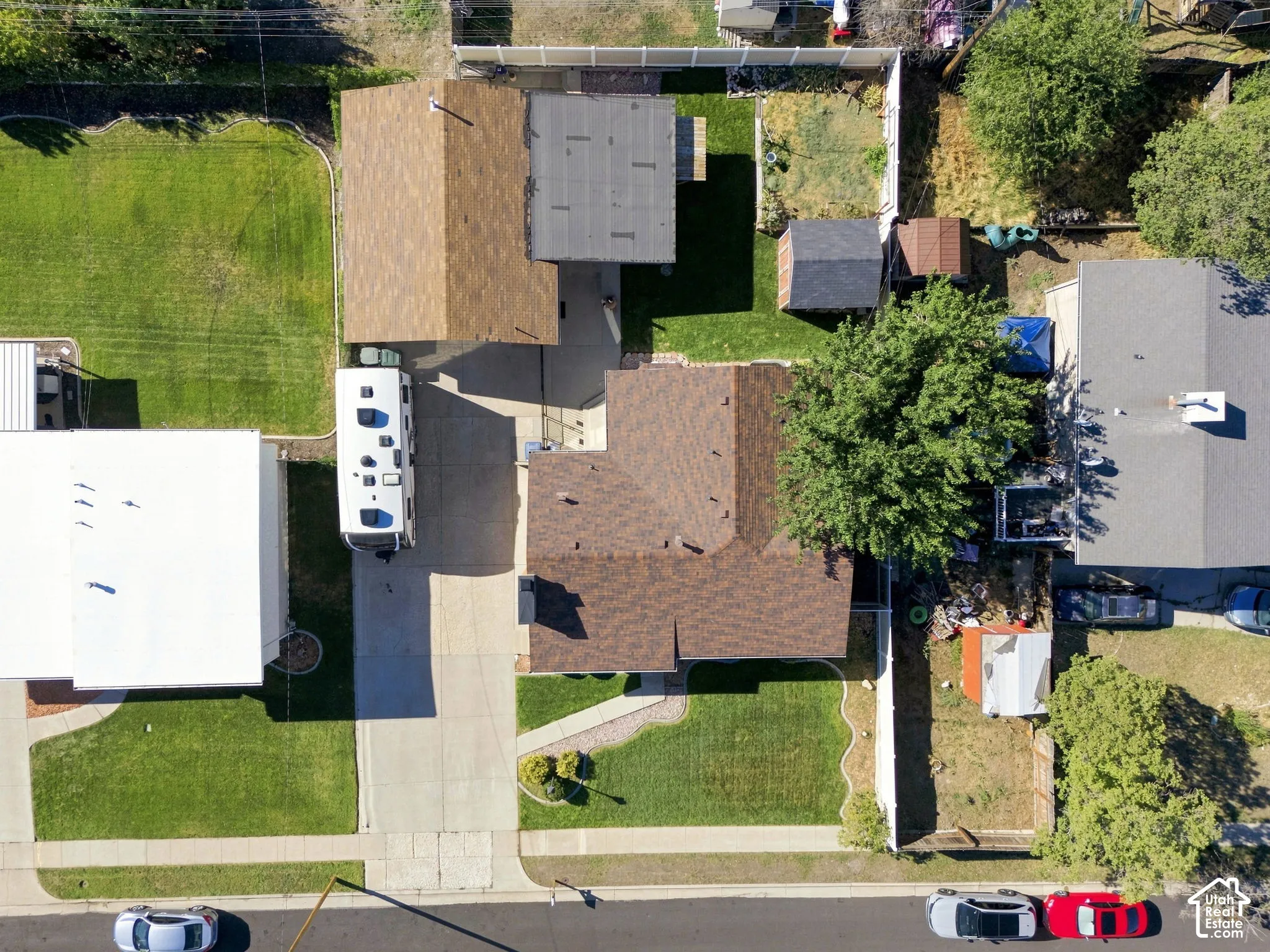 Brown shingle roof, paved driveway, green lawn, and fenced yard