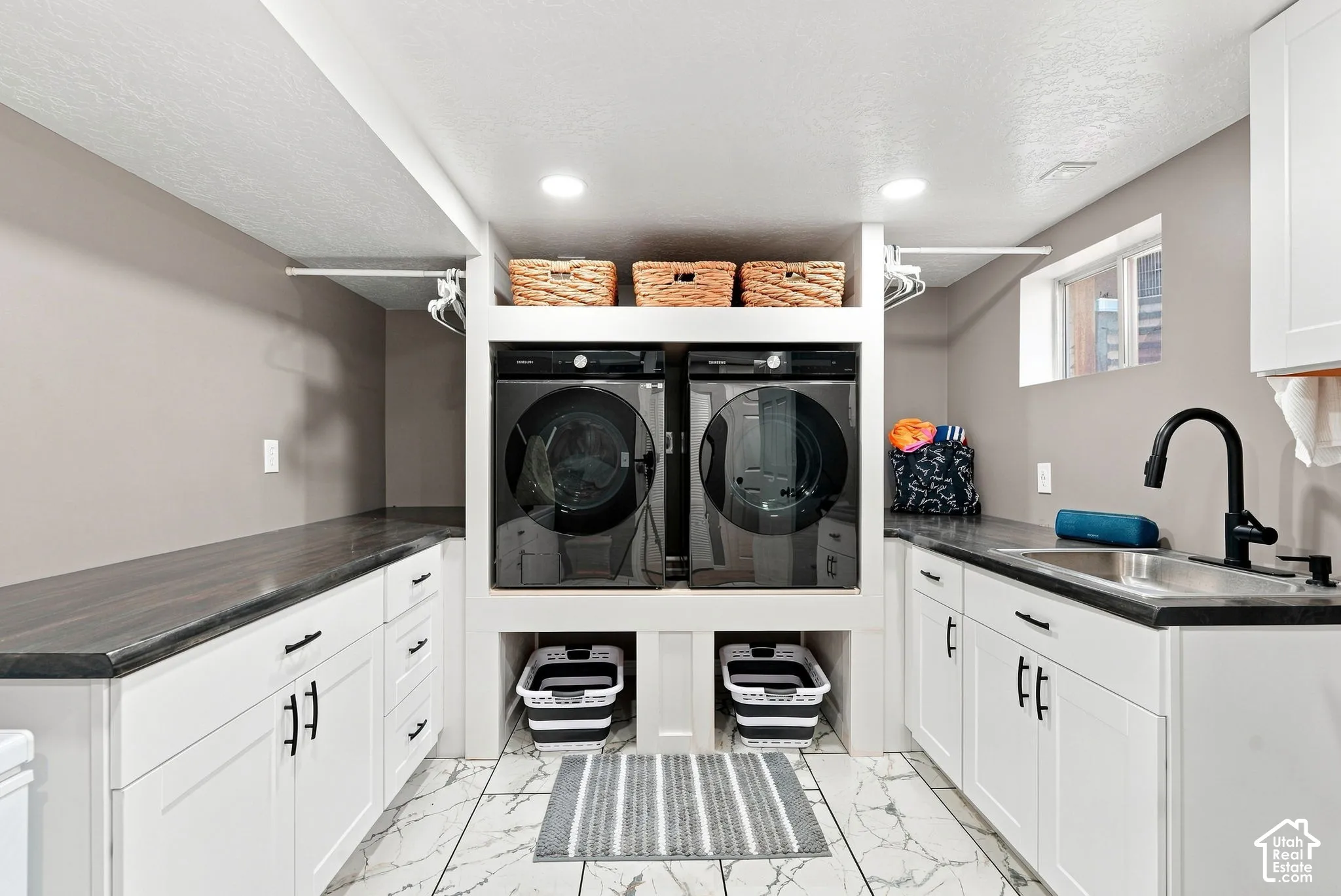 Laundry room featuring white cabinetry, dark countertops, a stainless steel sink, and a black faucet