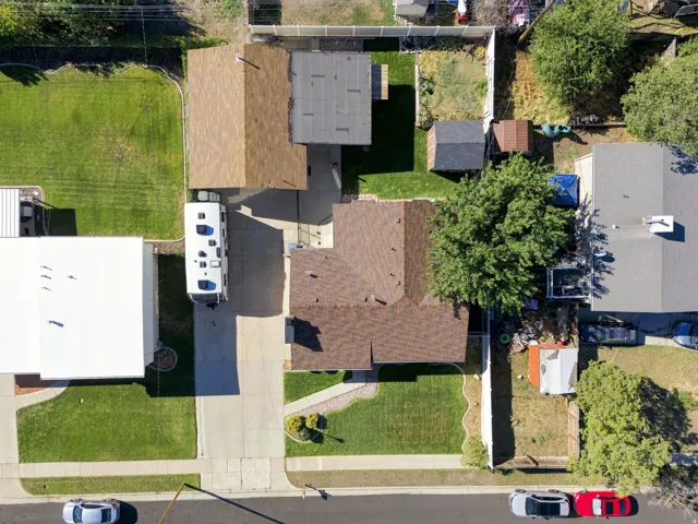 Brown shingle roof, paved driveway, green lawn, and fenced yard