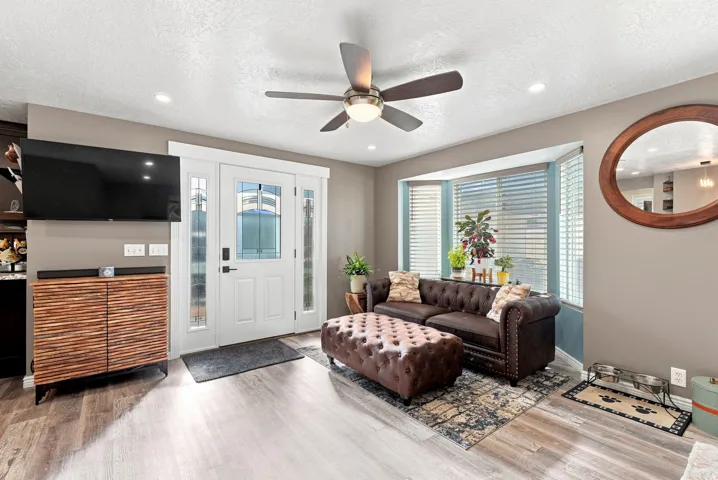 Recessed lighting, wood-finish flooring, a ceiling fan, a bay window with blinds, and a white entry door with frosted sidelights
