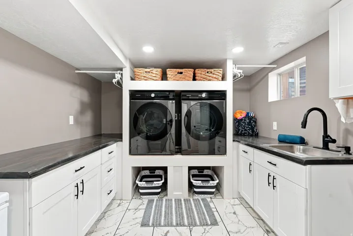 Laundry room featuring white cabinetry, dark countertops, a stainless steel sink, and a black faucet