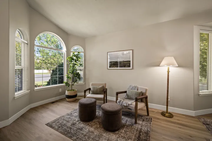 Vaulted ceiling, multiple arched windows, wood-finish flooring, neutral wall tones, and white trim