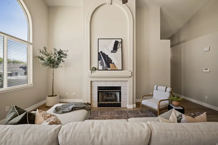 Living area featuring a vaulted ceiling, wood-finish flooring, a fireplace with a tiled surround, and a large arched window with blinds