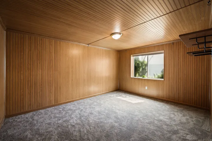 Paneling on walls and ceiling, wall-mounted light fixture, carpeted flooring, and a single window