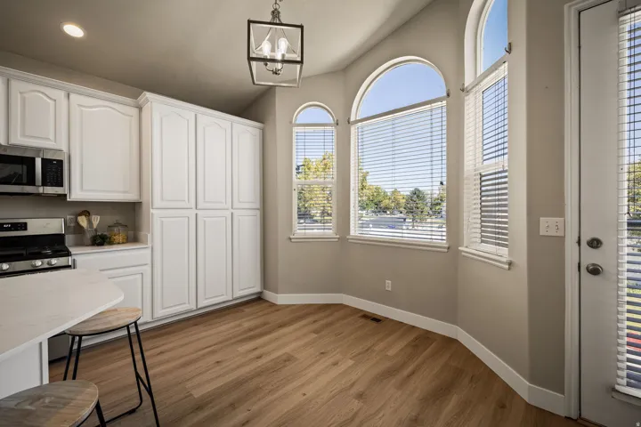 Arched windows, white cabinetry, wood-finish flooring, stainless steel appliances, and a black metal chandelier