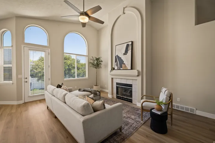 Vaulted ceiling with an illuminated ceiling fan, wood-finish flooring, and a fireplace with a mantel and tile surround
