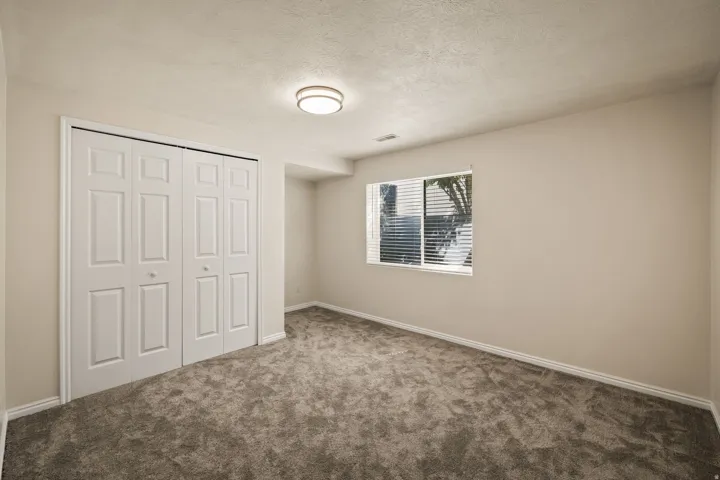 Neutral wall paint, plush carpet flooring, bi-fold closet doors, window with horizontal blinds, and a flush mount ceiling light fixture