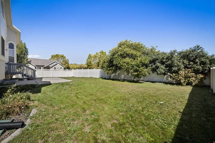 Expansive backyard featuring a concrete patio, a private white vinyl fence, and mature perimeter landscaping