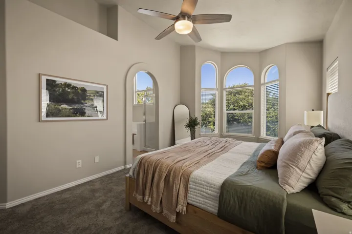 Recessed ceiling, arched doorway, bay window with arched transom windows, textured carpeting, and ceiling fan with integrated lighting