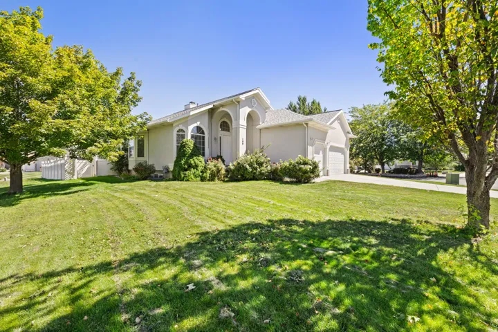 Pitched roof residence featuring a two-car garage, arched windows, and a manicured lawn with mature trees