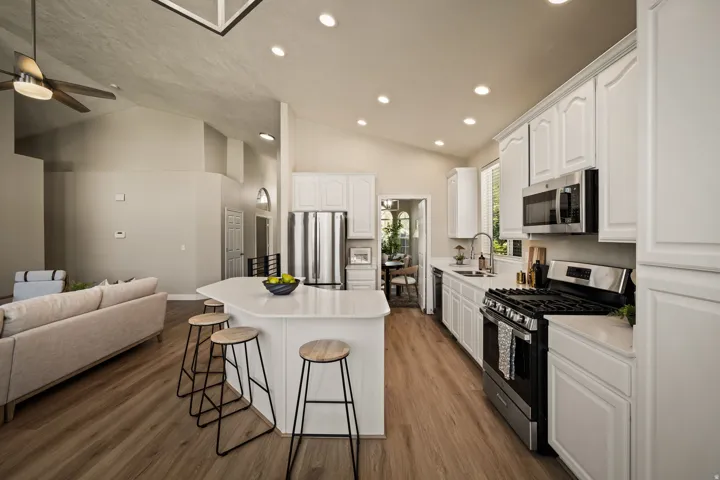 Vaulted ceilings with recessed lighting, wood-finish flooring, white cabinetry with stainless steel appliances, and a kitchen island with seating