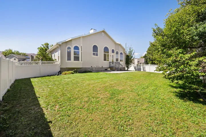 Expansive grass lawn with a white vinyl fence, mature trees, and a concrete patio