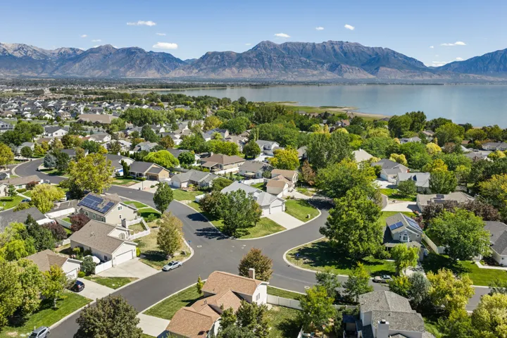Aerial perspective showcasing a residential neighborhood with mature trees, established landscaping, and mountain and water scenery