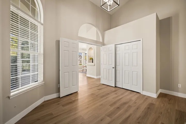 Vaulted ceiling with a geometric pendant light fixture, wood-finish flooring, arched doorway, and large window with blinds
