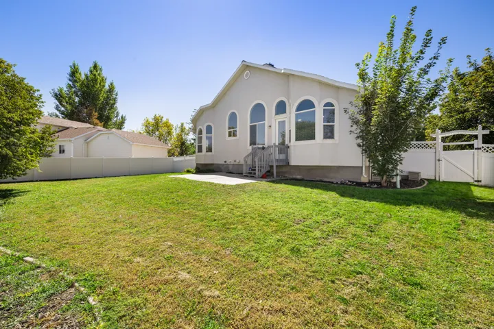Expansive backyard with a manicured lawn, concrete patio, and white privacy fencing