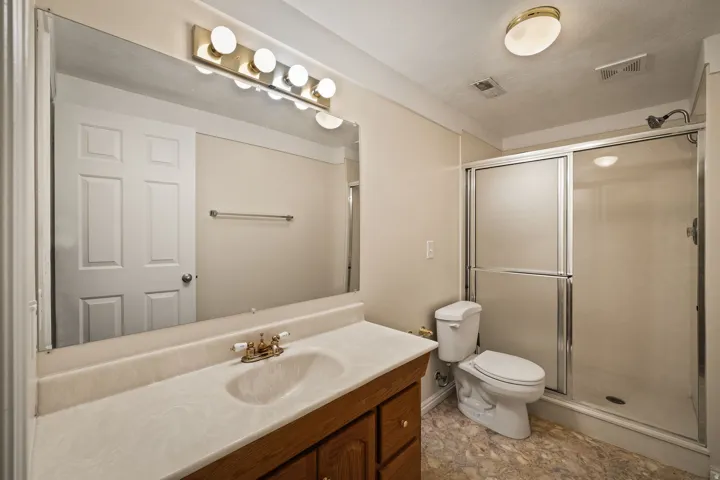 Vanity with a single basin, surface-mounted lighting, walk-in shower with sliding glass doors, and a built-in toilet