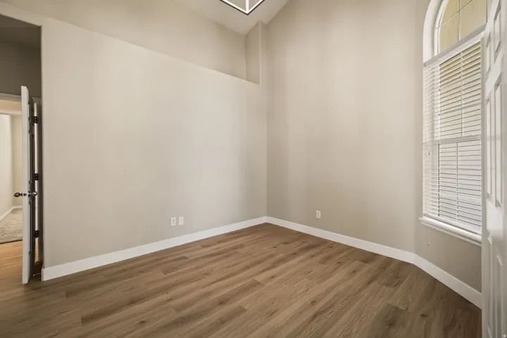 Room featuring wood-finish flooring, a wall-mounted arched window with blinds, and a white interior door