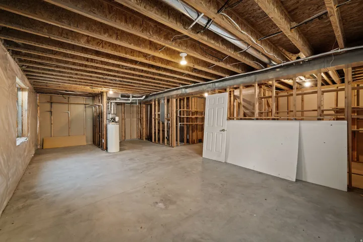 Unfinished basement featuring exposed wood joists, concrete flooring, and partial wood framing for future development