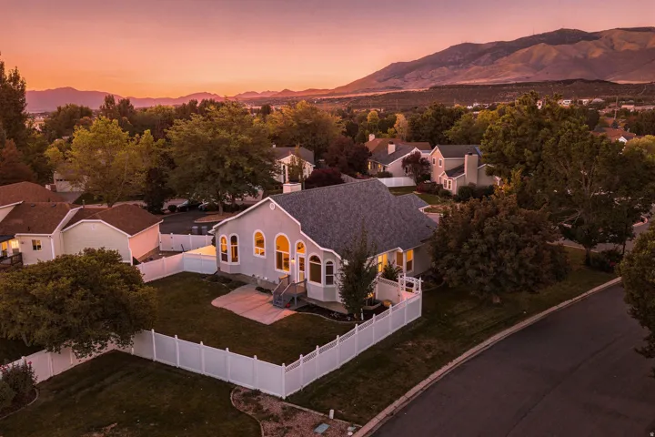 Light gray stucco exterior with arched windows, a white privacy fence, and an asphalt shingle roof